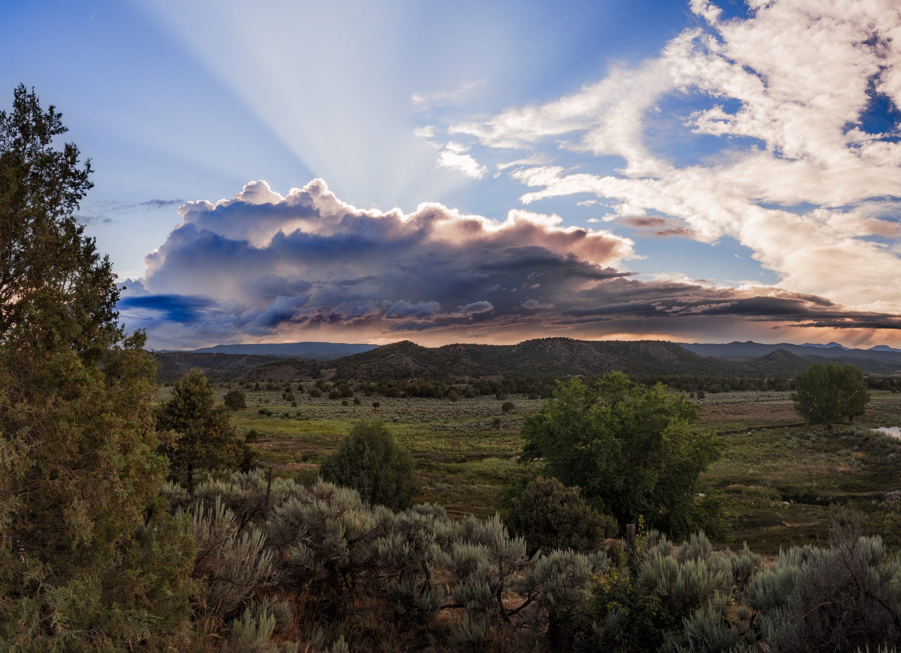 Sunbeams breaking through a heavy storm cloud over a sagebrush plain