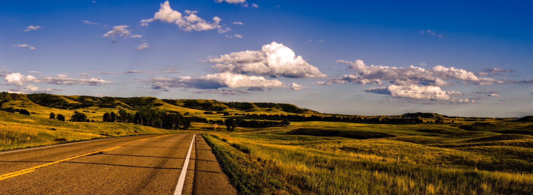 An empty two-lane road running straight through open prairie under a big sky