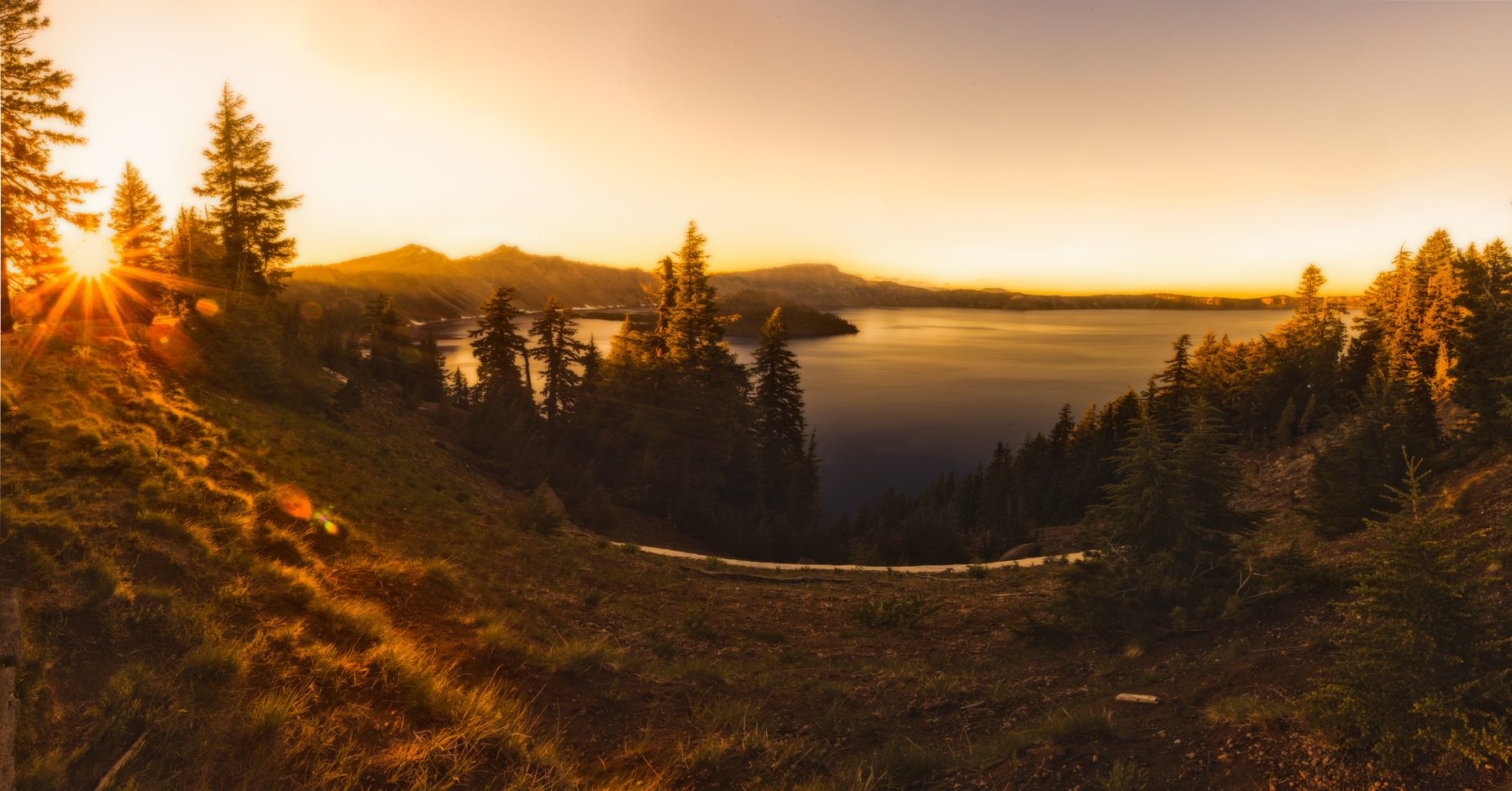 The sun bursting through trees on the rim above Crater Lake at sunset