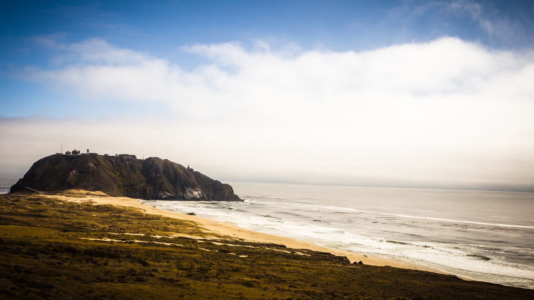 A coastal headland half-swallowed by fog above a long Pacific beach