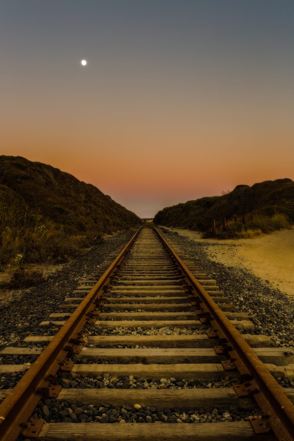 Railroad tracks running straight to the horizon under a rising moon at dusk