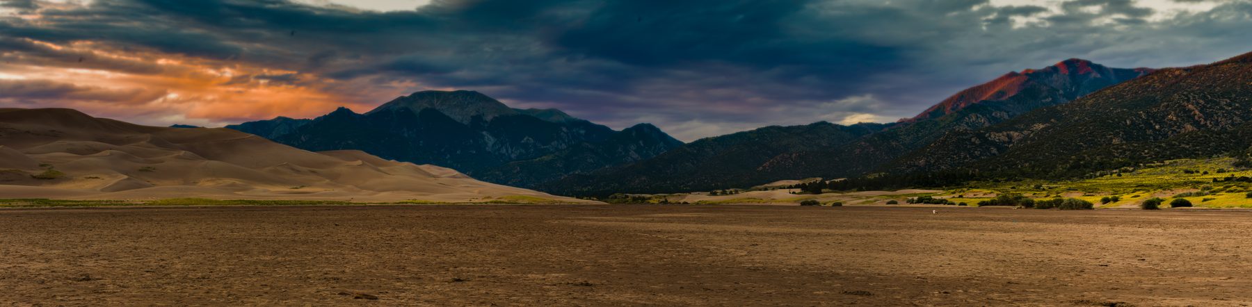 An ultra-wide view across an open valley floor to a distant mountain range
