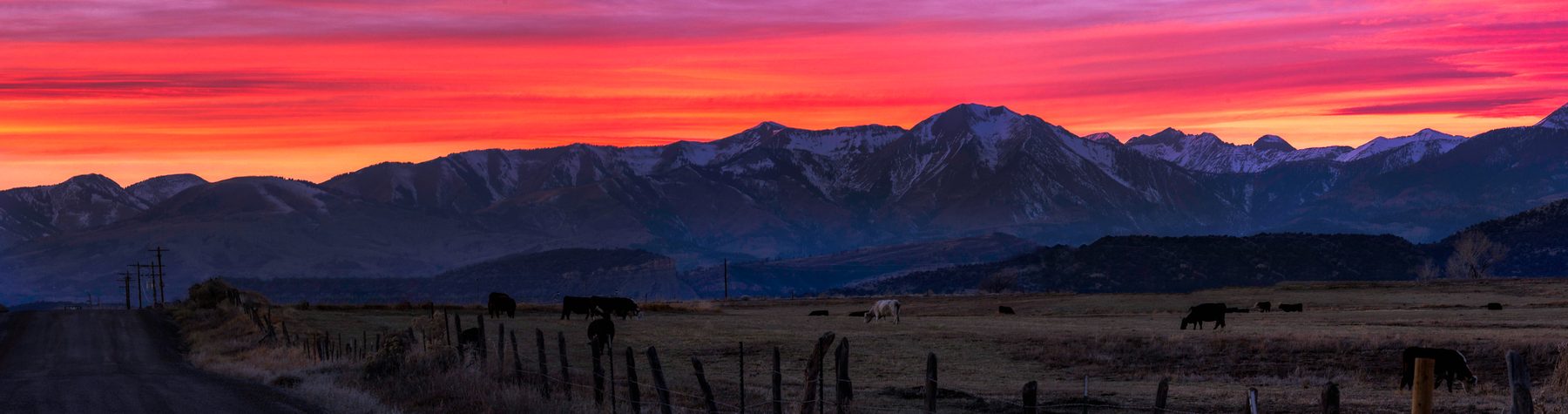 A band of red dawn cloud stretched over a dark mountain range and open range land