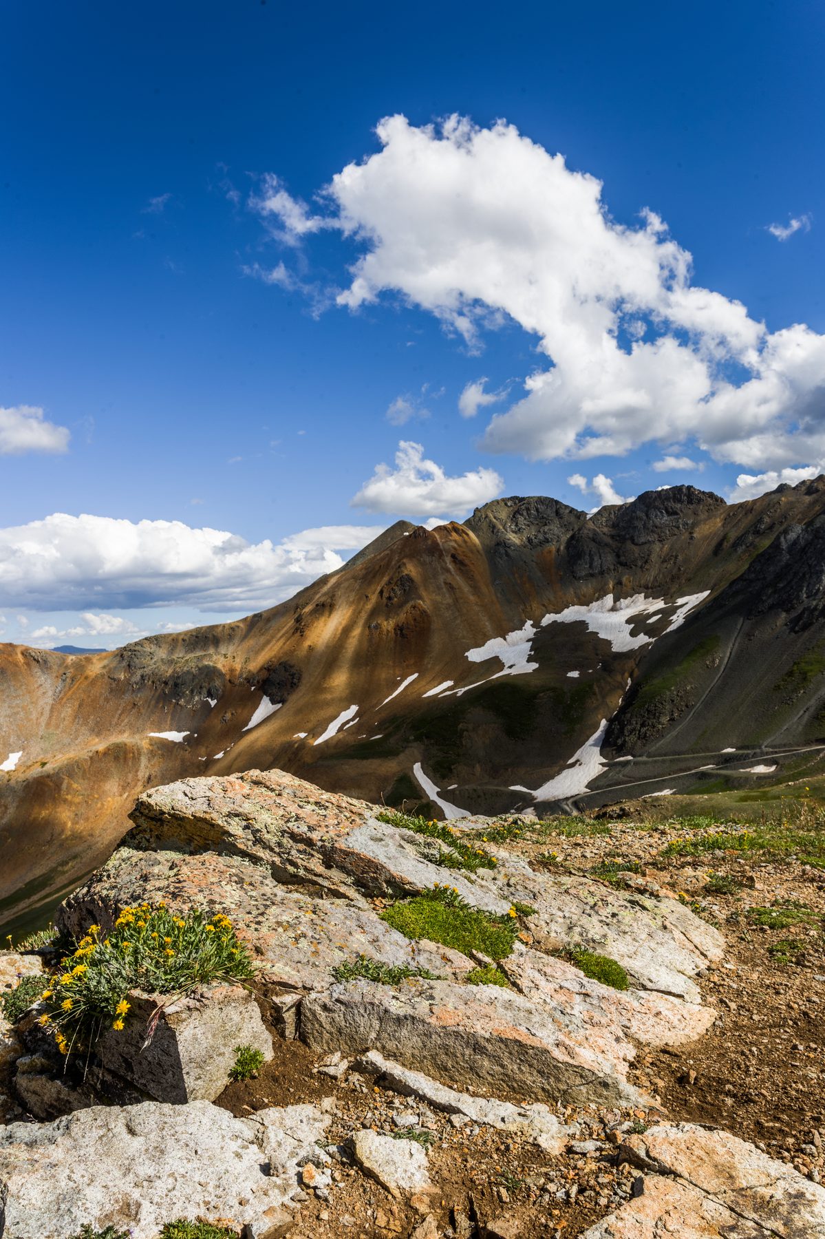 A rocky alpine ridge with lingering snow under a tall cumulus cloud