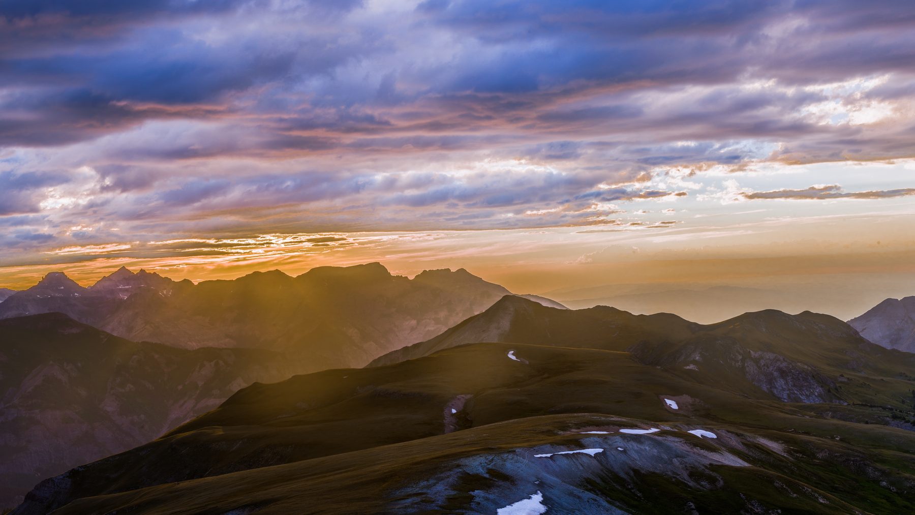 The sun breaking low across a series of alpine ridges at sunset