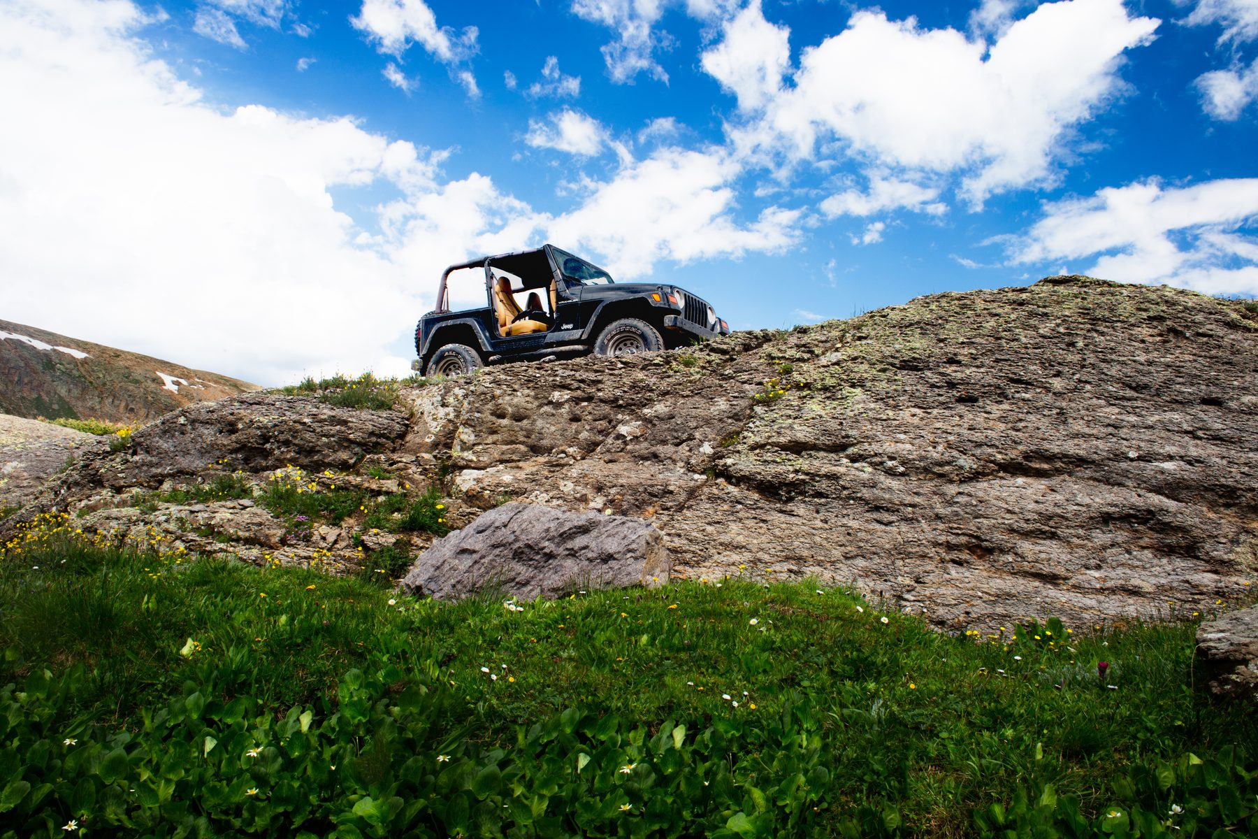 A Jeep parked on a rock outcrop high above a green alpine slope