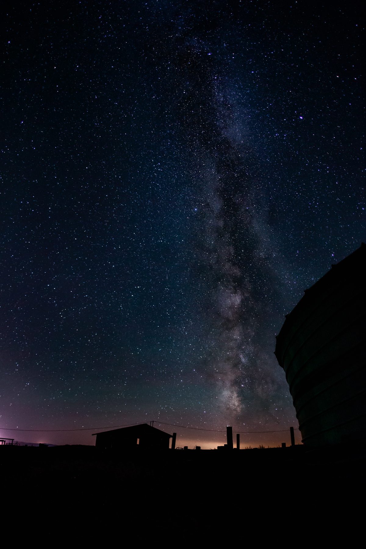 The Milky Way rising over a small dark cabin on an open plain