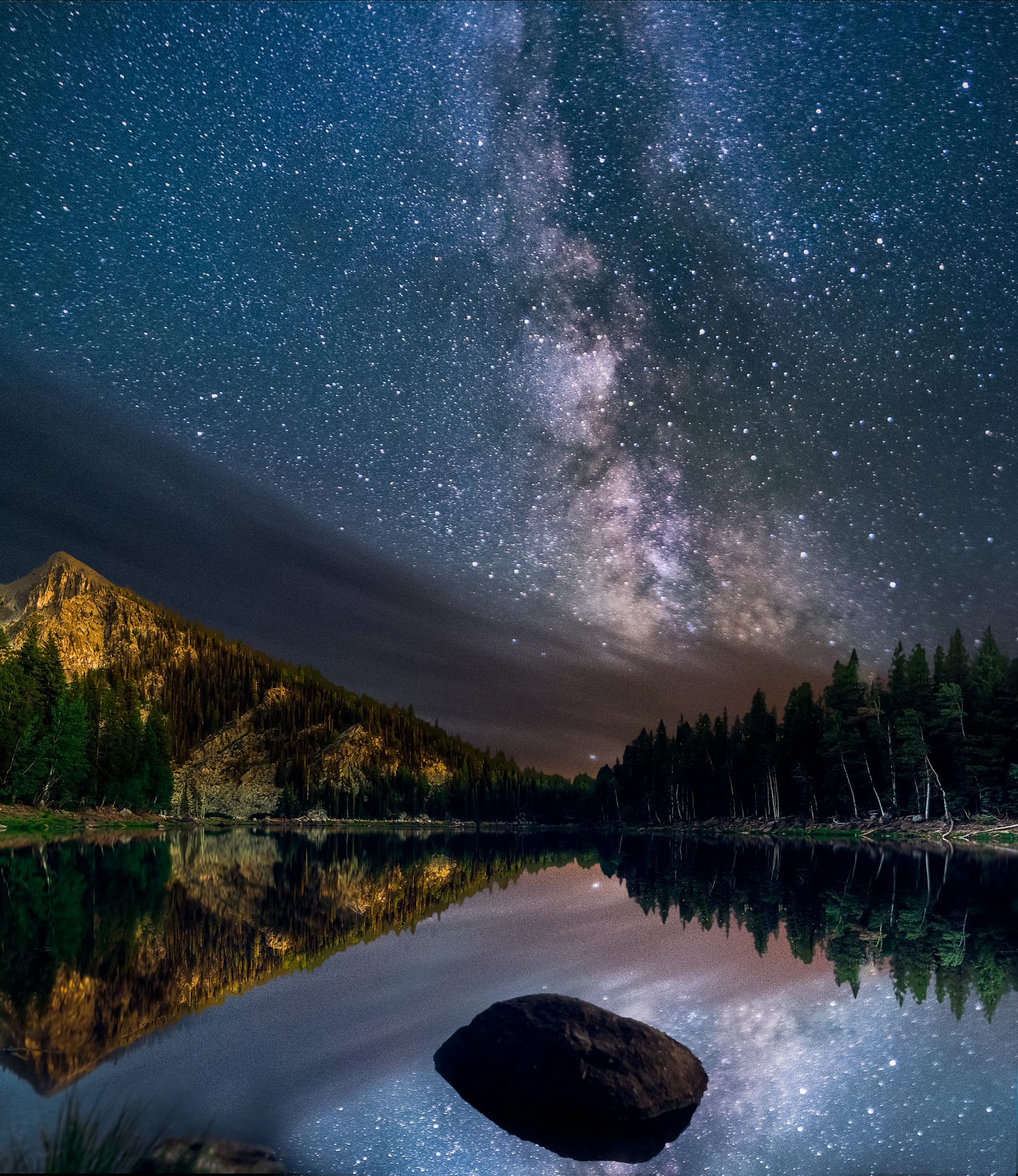 The Milky Way core over a mountain lake with a large boulder in the shallows