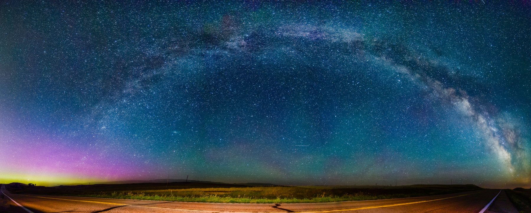 An ultra-wide panorama of the entire Milky Way arch over a flat dark horizon