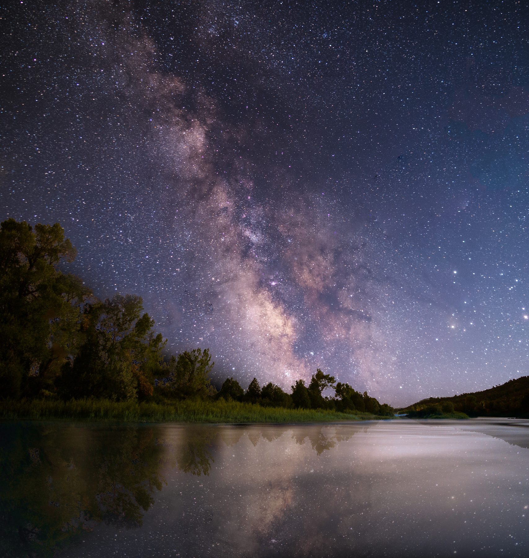 The Milky Way over a slow river, trees dark along the far bank