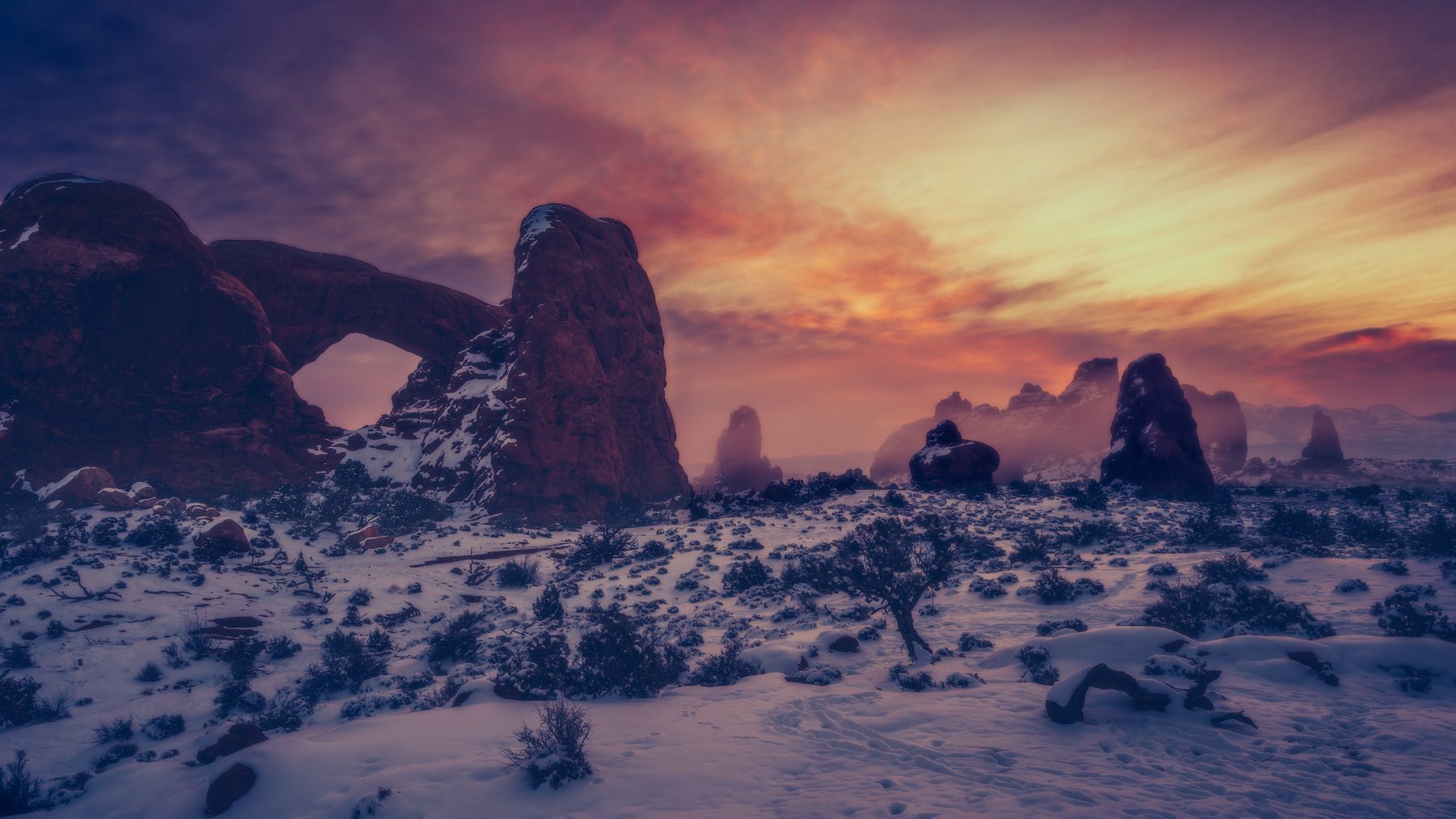 Turret Arch and the surrounding fins in snow under a streaked sunset sky
