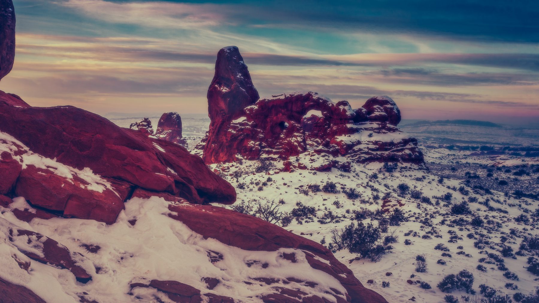 Turret Arch standing over snow-dusted red rock beneath a pale sky