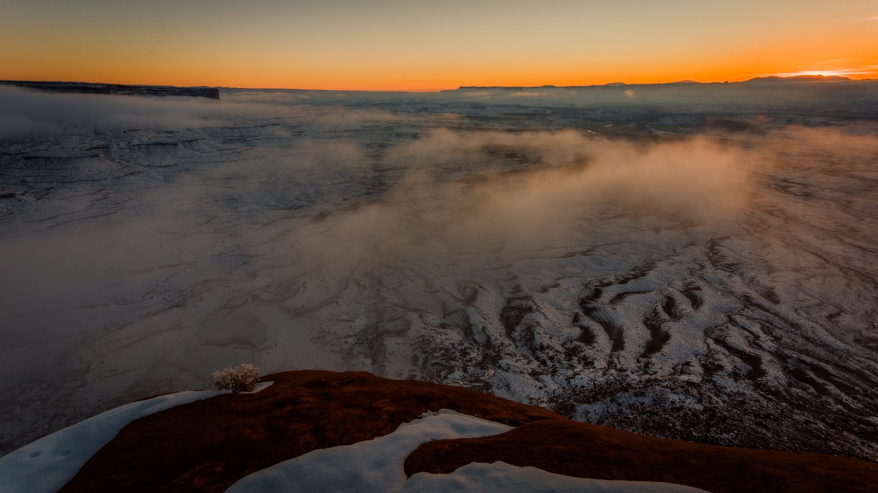 Fog pouring through a canyon system at sunrise, the rim edges catching light