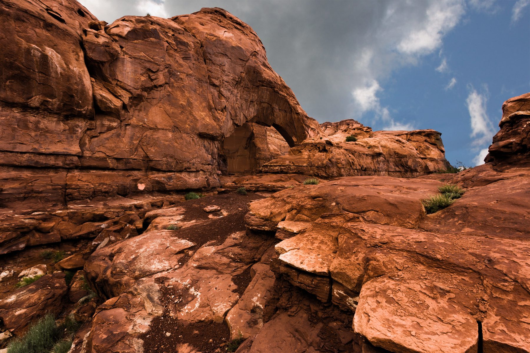Layered red sandstone ledges stepping up toward a bright cloud-scattered sky