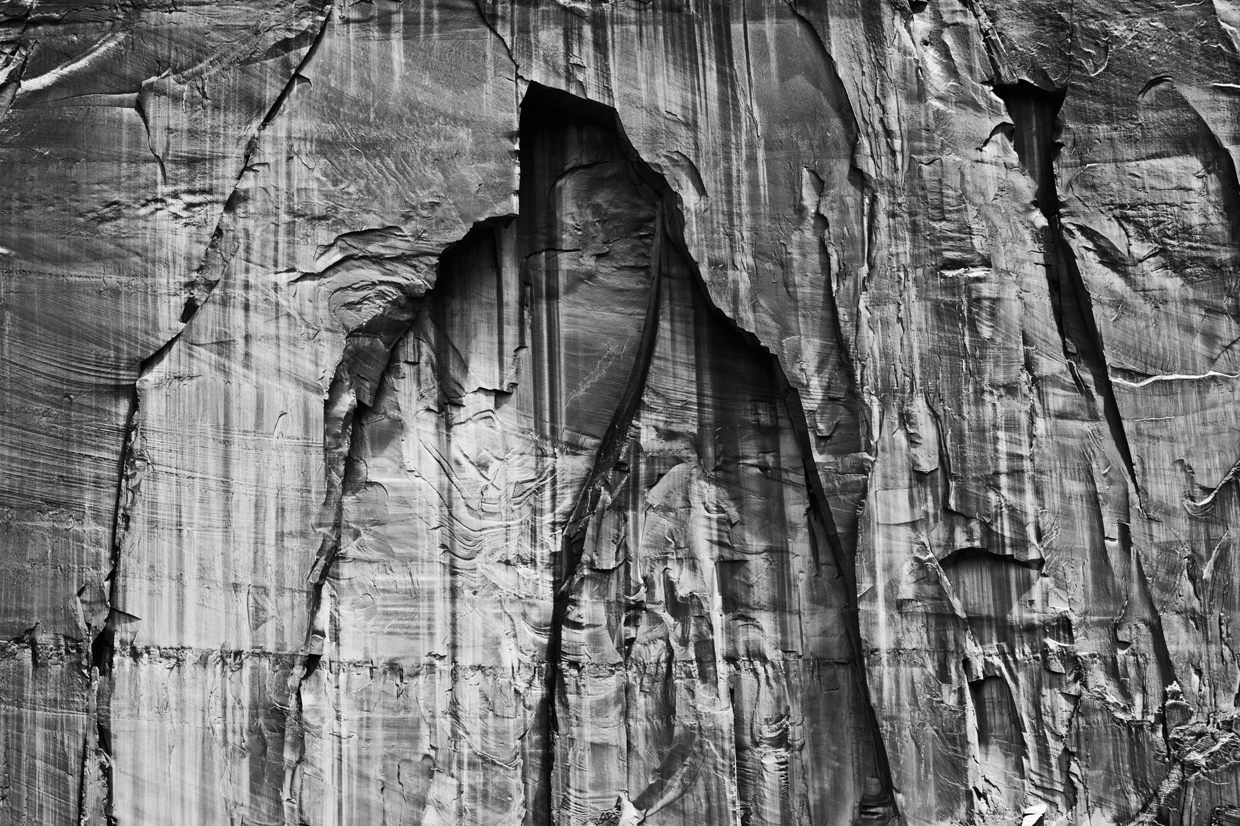 A black and white study of desert varnish streaking a tall sandstone wall