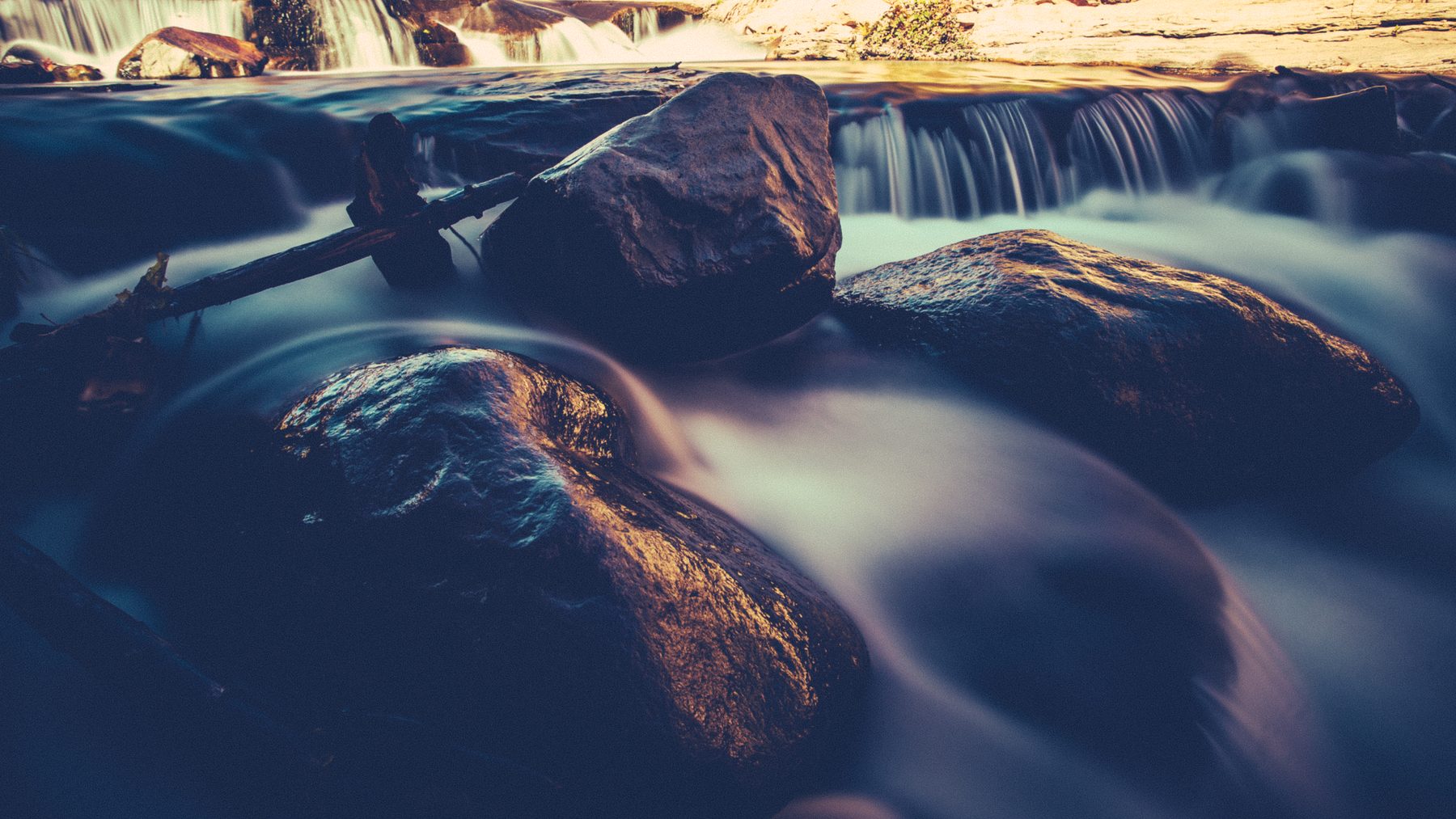 A long exposure of water sliding over rounded boulders in cool blue light