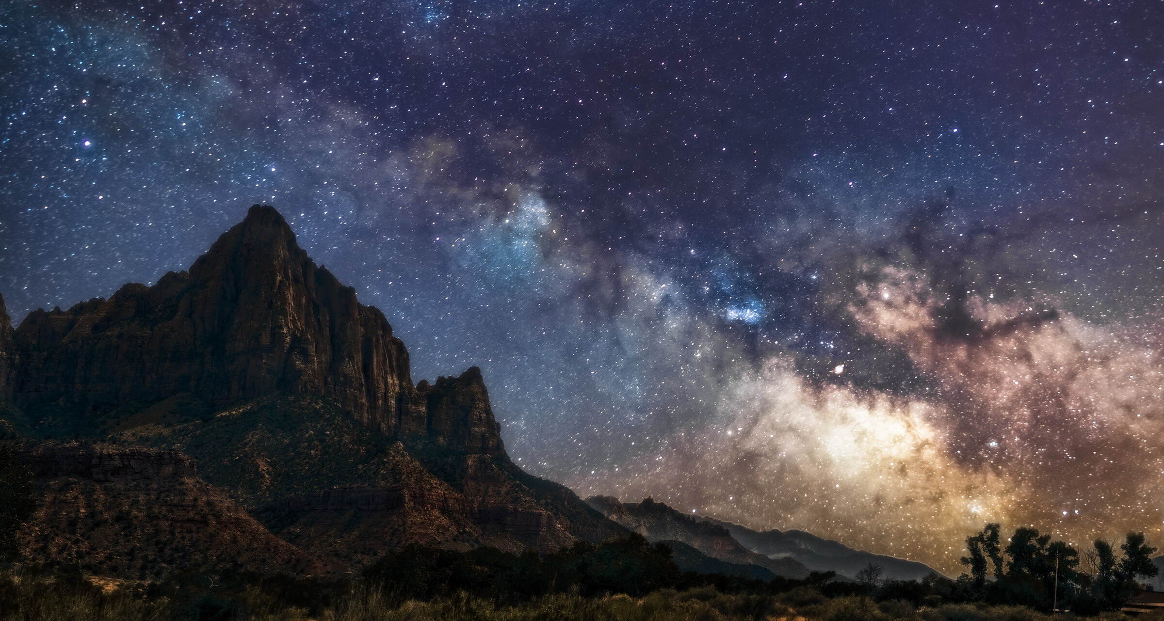 Milky Way galaxy core rising over the distinctive sandstone peak of The Watchman in Zion National Park, deep blue sky filled with stars